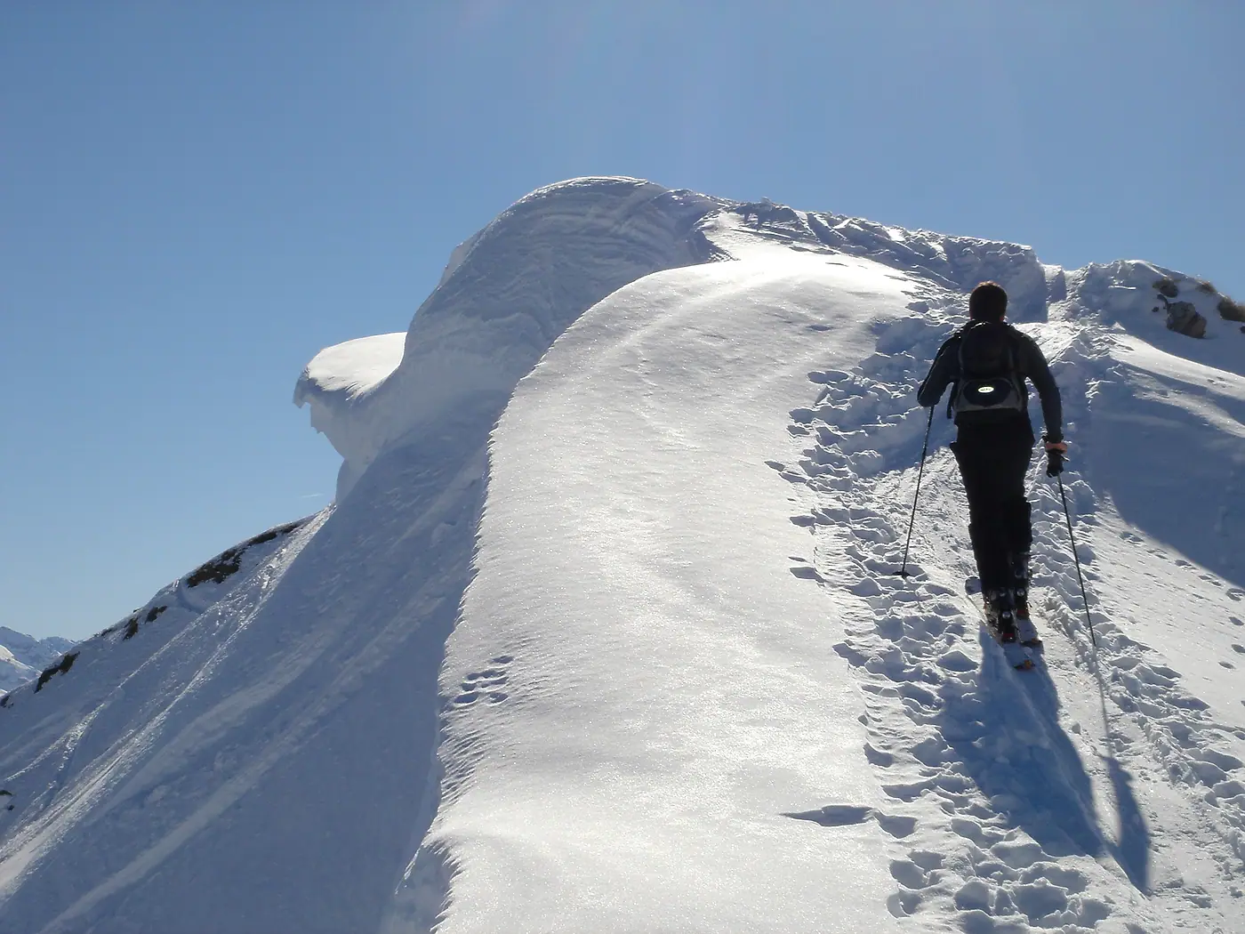 Ein Tourengeher steigt über einen verschneiten Grat zur Höferspitze, dahinter eine Schneewechte